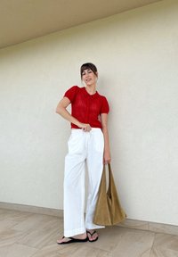 Bluză tricotată roșie cu mâneci scurte tip balon, asortată cu pantaloni largi albi și o geantă moale de culoare taupe. Sandalele negre completează ținuta.