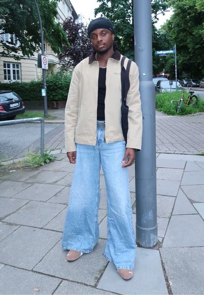 Chaqueta ligera beige sobre una camisa negra, combinada con unos vaqueros de denim azul claro de gran tamaño y zapatos beige. Bandolera negra.