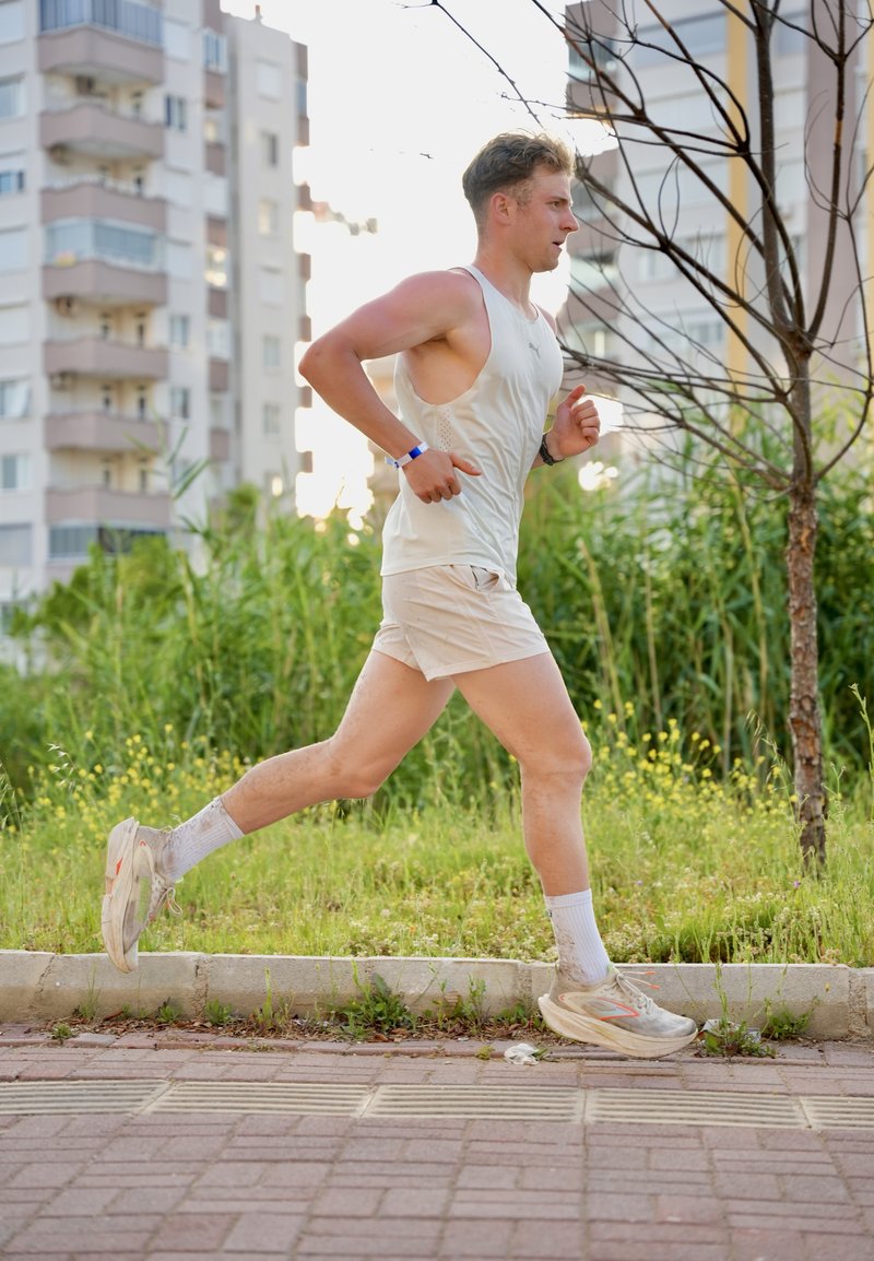 Jeune homme courant en plein air sur un chemin pavé près de l'herbe et des bâtiments, portant des vêtements de sport légers et des baskets.