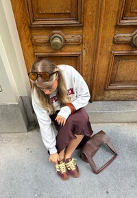 Sportowe buty w kolorze burgundowym i brązowym z żółtymi sznurówkami; noszące szare sweter oraz burgundową spódnicę. Obok brązowa torebka.
