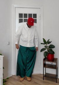 Cămașă albă cu mâneci lungi, cu croială oversized, asorată cu pantaloni verzi largi din satin, având dungi albe pe laterale. O pălărie roșie și saboți bej completează ținuta.