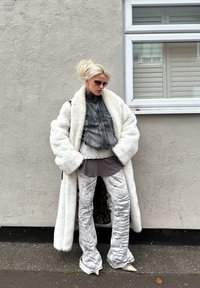 Bílý kabát z umělé kožešiny, krátká šedá džínová bunda, šedá tunika, stříbrné lesklé zvonové kalhoty, bílé boty na špičku a sluneční brýle.