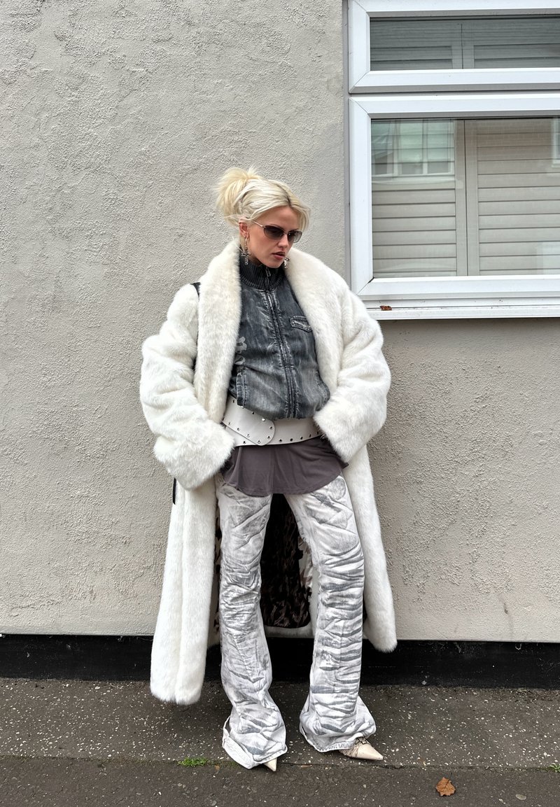 Witte nep bontjas, grijs denim jasje in cropped model, grijze tuniek, metalen zilverkleurige uitlopende broek, witte puntige laarzen en een zonnebril.