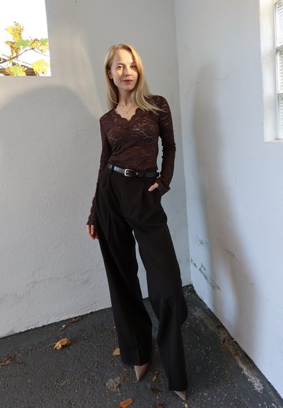 Top marrón de encaje con mangas largas y escote ondulado, combinado con pantalones negros de talle alto y tacones beige puntiagudos. Incluye un cinturón negro sencillo.