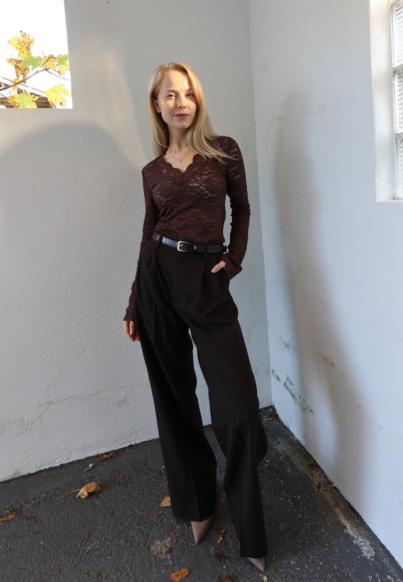 Brun blonder langærmet top med bølget halsudskæring, kombineret med højtaljede sorte bukser og beige spidse hæle. Enkel sort bælte medfølger.