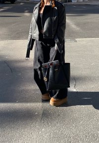 Zwarte leren jasje over een zwarte crop top, wijde zwarte broek, tan platform schoenen en een zwart gestructureerde handtas met een gouden hanger.
