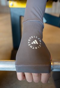 Marrón, manga atlética ajustada con logo, diseño entallado, textura suave, que llega hasta la muñeca, sujetando una barra de pesas metálica texturizada.