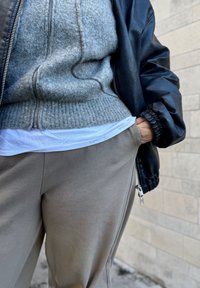 Szary sweter z dzianiny pod czarną skórzaną kurtką typu bomber, w połączeniu z khaki spodniami, wyposażonymi w boczną kieszeń i prążkowany mankiet.