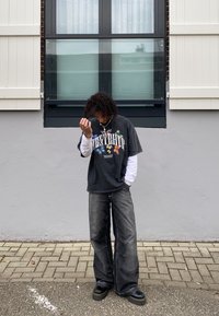 Μαύρη γραφική μπλούζα t-shirt με πολύχρωμο σχέδιο πεταλούδας, τοποθετημένη πάνω από ένα λευκό μακρύ μανίκι μπλουζάκι. Σκοτεινά φαρδιά τζιν και χοντρές μαύρες πλατ�φόρμες.