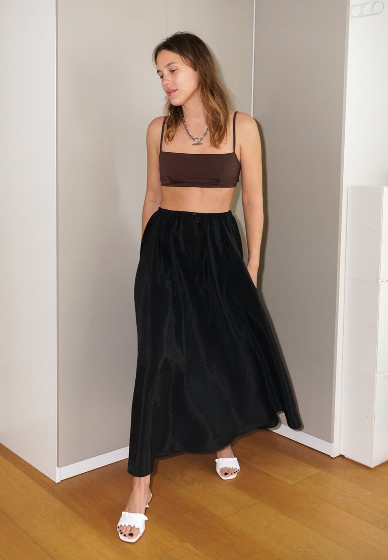 Ruskea crop-top, johon on yhdistetty pitkä, liehuva musta hame. Hameessa on sileä pinta ja se istuu vyötäröllä, ja sen kanssa on valkoiset korkokenkiä.