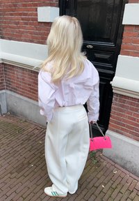 Biele nohavice s širokými nohavicami, svetloružová pruhovaná košeľa s mašľou a malá ružová kabelka. Pohľad dopĺňajú tenisky so zelenými pruhmi.