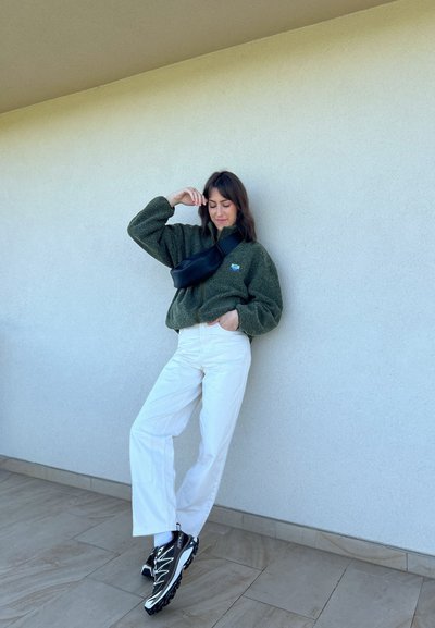 Chaqueta de forro polar verde con cuello con cremallera, combinada con pantalones de pierna ancha blancos y zapatillas deportivas negras, que incluyen un bolso cruzado negro.