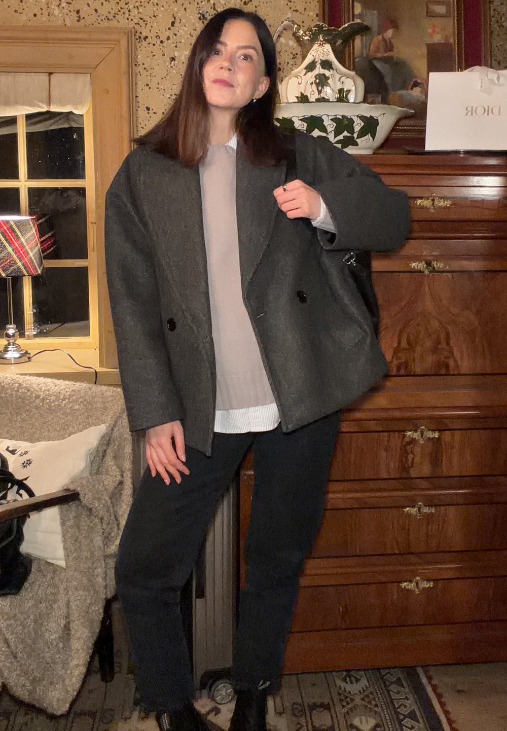 Veste surdimensionnée en mélange de laine grise avec double boutonnière, portée sur un haut beige et une chemise blanche, associée à un pantalon noir et des bottes.