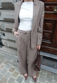 Kreemina pinstripesümpelühe valge vormitud pluusi peal, koos laihõlmse kreemika püksega. Kaasas väike pruunast nahkväike kott ja teravade pruunide kontsadega kingad.