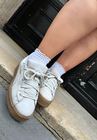 Grijze leren sneakers met een gestructureerde, lichtbruine plateauzool, gekenmerkt door beige veters en metallic accenten. Witte gerimpelde sokken zichtbaar.