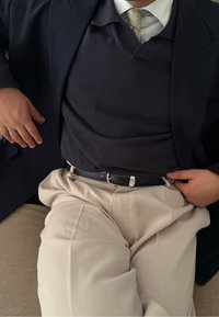 Ναυτικό μπλέιζερ πάνω από ένα ναυτικό πουλόβερ, λευκό πουκάμισο και μπεζ παντελόνι. Μαύρη ζώνη με ασημί λεπτομέρειες συγκρατεί το παντελόνι στη μέση. Χαλαρή καθιστή στάση.