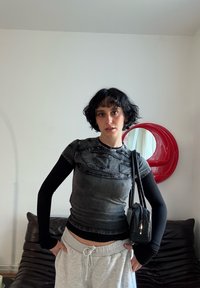 Haut ajusté noir et gris avec un motif texturé, manches longues, associé à un pantalon de jogging gris et un petit sac à main noir. Miroir circulaire rouge en arrière-plan.