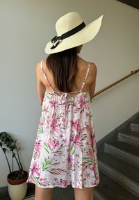 Λευκό, αμάνικο φόρεμα με λουλουδάτα μοτίβα σε ροζ και πράσινο, διαθέτει φιόγκο στην πλάτη. Ένα καπέλο από άχυρο με φαρδύ γείσο και μαύρη κορδέλα.