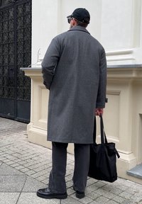 Cappotto di lana grigio, pantaloni grigio scuro, scarpe nere e una borsa tote nera. Vista posteriore con coppola e occhiali da sole.