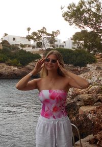 Strapless badpak met een roze bloemenpatroon, gecombineerd met witte linnen shorts. De achtergrond toont een rotsachtige kustlijn en witte gebouwen.