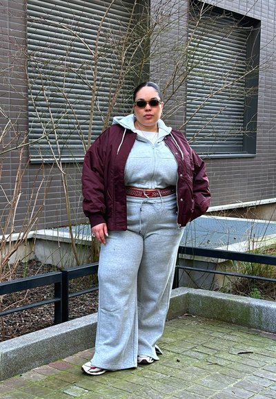 Chaqueta bomber burdeos sobre un hoodie gris y pantalones de chándal de pierna ancha a juego. Zapatillas deportivas blancas con un sutil patrón de rayas.