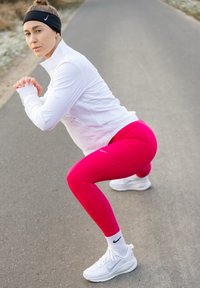 Ensemble sportif pour femme comprenant un haut blanc à manches longues et des leggings rose vif. Les accessoires incluent un bandeau noir et des baskets blanches.