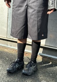 Μαύρο κοντό παντελόνι γόνατος από ανθεκτικό ύφασμα, συνδυασμένο με μαύρες κάλτσες γόνατος και μαύρα αθλητικά παπούτσια με υφή και κορδόνια.