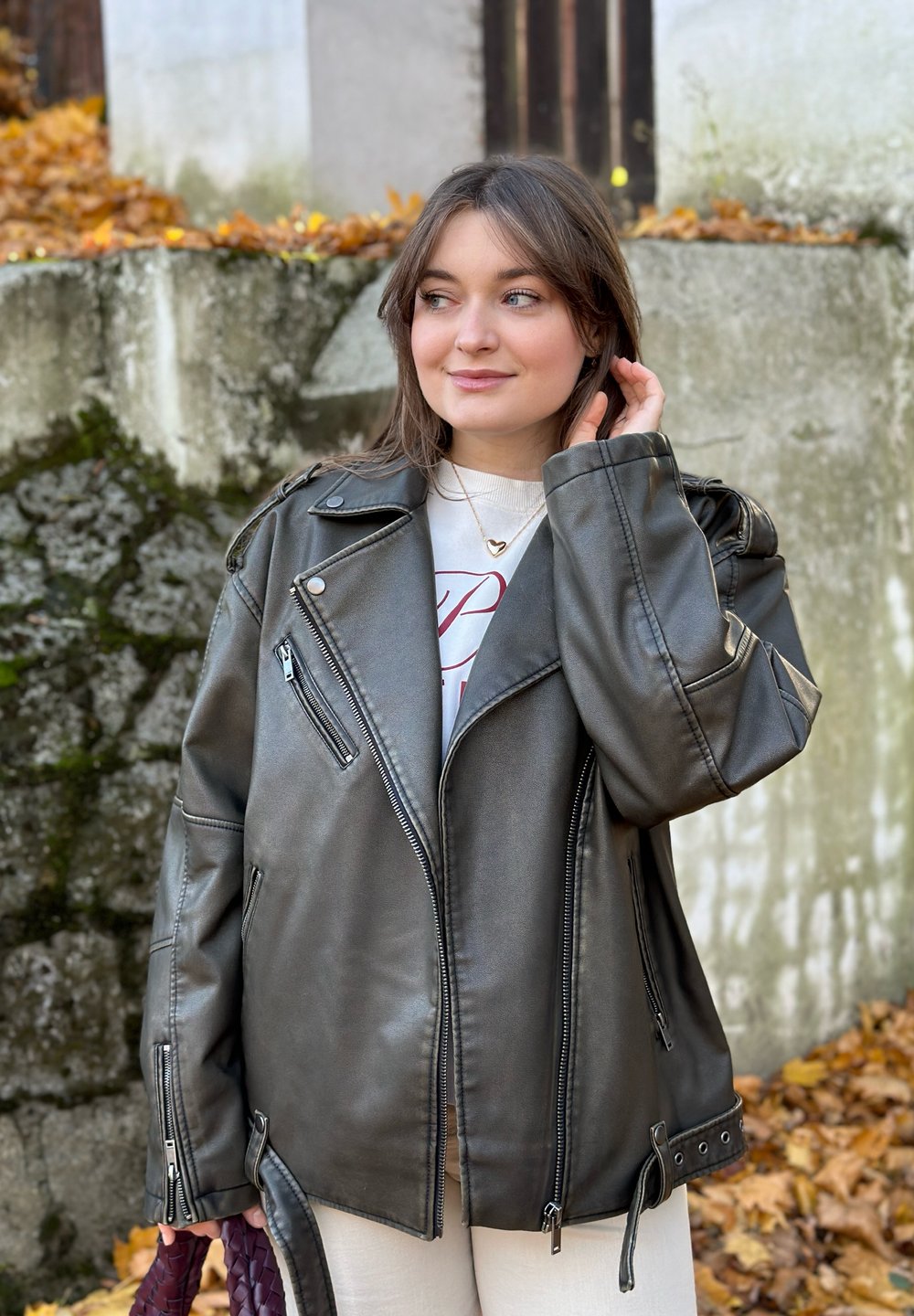 Veste de moto en simili cuir noir avec quincaillerie argentée, fermetures éclair et large col. Elle possède des épaules tombantes et deux poches latérales.
