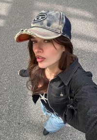 Džínová šiltovka s opotrebovaným okrajom, čierna džínová bunda, čierne tričko, svetlomodré džínsy, strieborný n�áhrdelník a čierna taška.