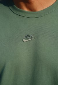Világoszöld pamut póló bordázott kerek nyakkivágással és sötétzöld hímzett Nike logóval a bal mellen. Simát tapintású.