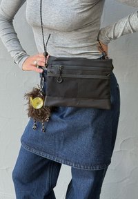 Sac bandoulière noir en matériau texturé avec panneau en maille, doté de deux poches zippées et d'un porte-clés en fourrure attaché avec un charme jaune.