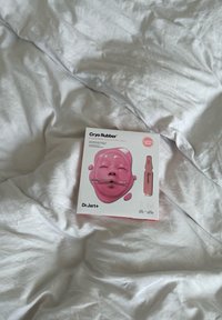 Emballage du masque raffermissant Cryo Rubber de Dr.Jart+ sur des draps blancs froissés, avec une illustration de masque facial rose.