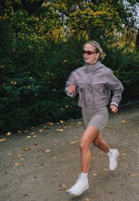 Grå atletisk jacka med hög krage, tillsammans med åtsittande grå shorts med vita detaljer. Löpare i vita sneakers med en texturerad design.