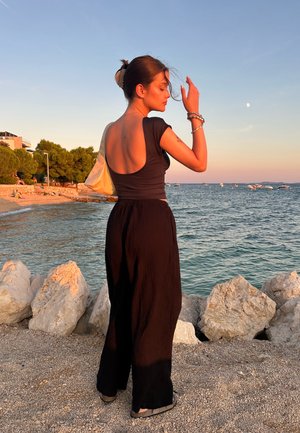 Pantalones anchos de cuadros negros y una blusa ajustada oscura con la espalda al descubierto. Un bolso beige y joyería de plata complementan el atuendo.