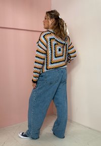 Suéter colorido em estilo crochê com um padrão quadrado em tons pasteis; combinado com jeans azul claro, soltos, e ténis pretos.