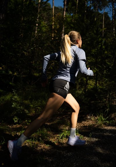 Ropa atlética: una camiseta de manga larga de color azul claro y pantalones cortos negros con rayas blancas. Las zapatillas de correr son lilas con acentos rojos, usadas con calcetines blancos.