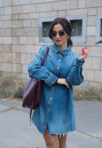 Džinsa krekla kleita ar garām piedurknēm, pogas priekšpusē un frēzētu apakšu. Valkāta ar bordo krāsas plecu somu un apaļām saulesbrillēm.