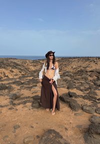 Brun maxi skjørt med høyt splitt, hvit gjennomsiktig skjorte og dyreprint-bikini topp. Tilbehør inkluderer en brun hatt og solbriller.
