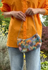 Bolsa de mão com contas, apresentando várias cores, padrões intrincados e uma alça de corrente prateada. Forma suave e arredondada, com uma superfície texturizada.