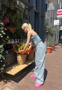 Denim outfit with a strapless top and wide-leg pants, paired with bright pink platform sandals. Two woven baskets hold colorful flowers.