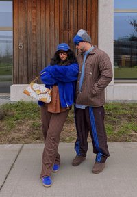 Un cappotto in pelliccia sintetica blu, una giacca trapuntata marrone, pantaloni rigati marroni e accessori blu. Borsa a fantasia notevole e sneakers blu.