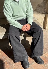 Ljusgrön fluffig tröja med krage, kombinerad med lösa svarta jeans och svarta skoslip-ins. Sitter på en stenbänk.