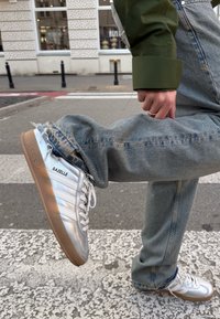 Srebrni usnjeni superge z belimi vezalkami, v retro dizajnu in bež podplatom. V kombinaciji z zbledelimi modrimi džinsom, nekoliko raztrganimi na robu.