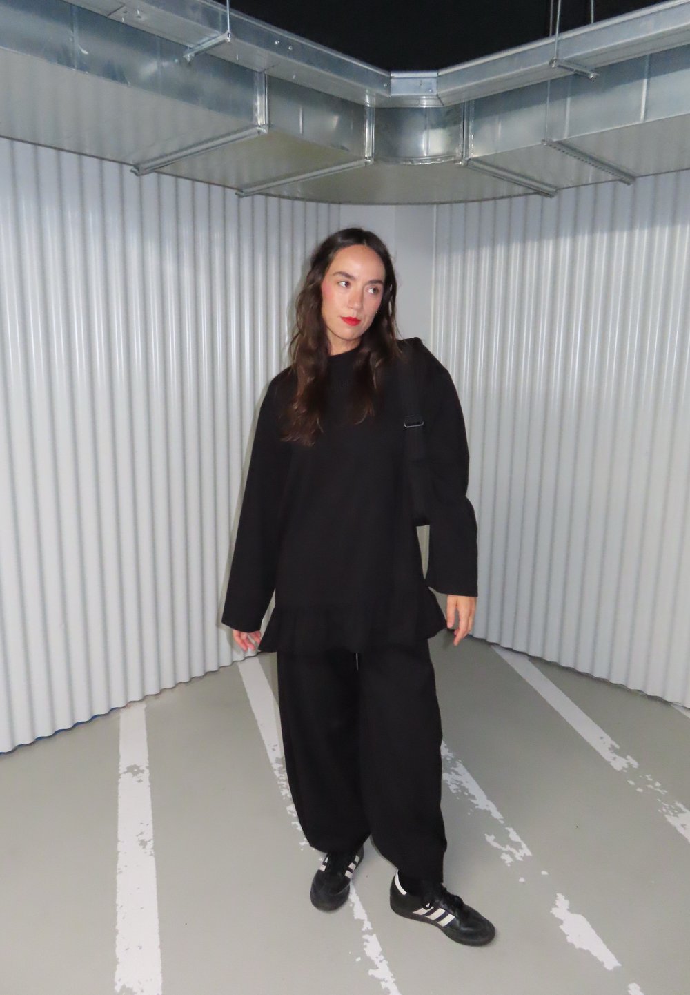 Čierne oversized tričko s volánikovým lemom, skombinované s voľnými čiernymi nohavicami. Nosí sa s čiernymi teniskami s tromi bielymi pruhmi.