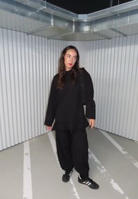Čierne oversized tričko s volánikovým lemom, skombinované s voľnými čiernymi nohavicami. Nosí sa s čiernymi teniskami s tromi bielymi pruhmi.