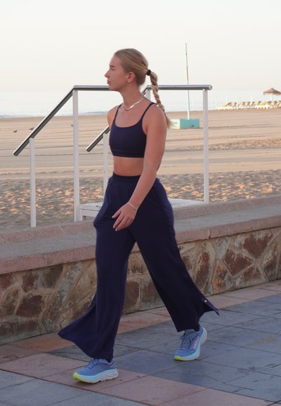 Top corto azul marino y pantalones de pierna ancha de tejido ligero. Caminando por un camino pavimentado, combinados con zapatillas deportivas azules con acentos neón.