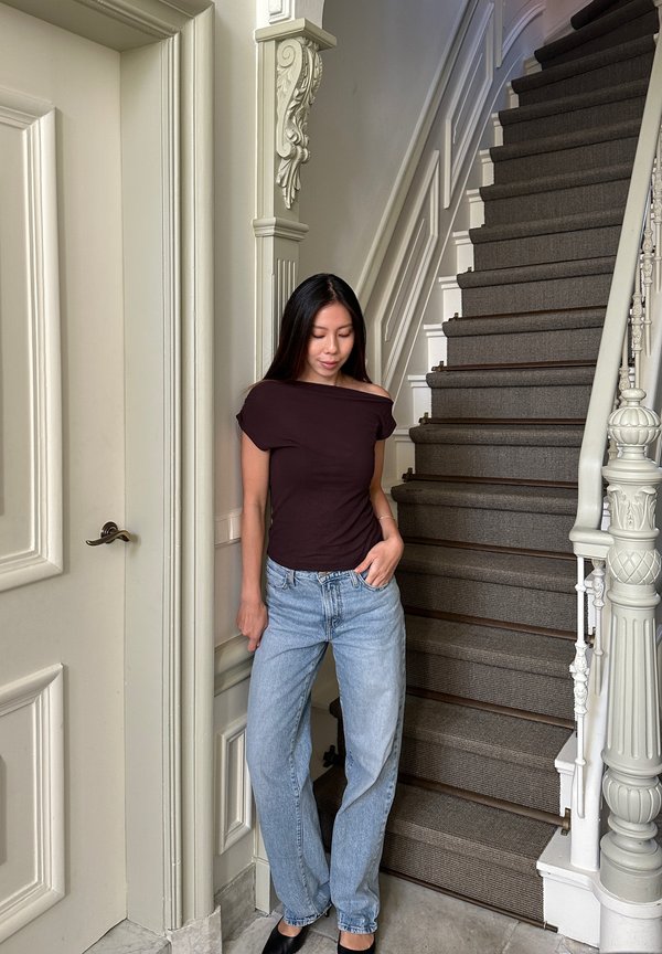 Djupt lila topp utan axlar i kombination med ljusblå jeans med rak ben. Står på en trappa med texturerade bruna steg och utsmyckat räcke.