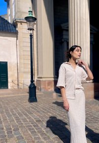 Ensemble deux pièces beige clair comprenant un haut à col et à manches courtes avec des boutons, et une longue jupe ajustée, tous deux ornés de motifs texturés.