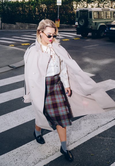 Trench rosa claro, blusa blanca con detalles de ojal, falda de cuadro en rojo, verde y negro, calcetas grises y mocasines negros.