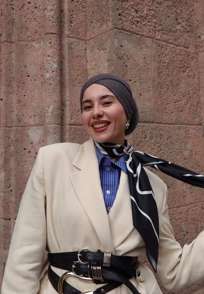 Blazer beige de gran tamaño sobre una camisa a rayas azul, accessorized con una bufanda negra con patrones blancos y un cinturón negro grueso con herrajes plateados.